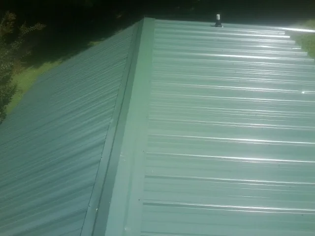 New green metal panels meeting at the ridge of a roof — Flat Roof Repair work by our crew in Crescent